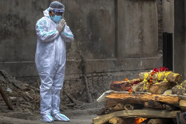 A relative in protective suit performs last rituals as the body of a person who died of COVID-19 is cremated in Gauhati, India, Monday, May 24, 2021. (Photo by Anupam Nath/AP Photo)