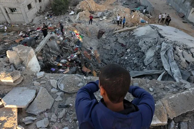 A young boy looks on as people check the rubble of a building destroyed in an Israeli bombardment in Rafah in the southern Gaza Strip on October 21, 2023. Thousands of people, both Israeli and Palestinians have died since October 7, 2023, after Palestinian Hamas militants based in the Gaza Strip, entered southern Israel in a surprise attack leading Israel to declare war on Hamas in Gaza on October 8. (Photo by Mohammed Abed/AFP Photo)
