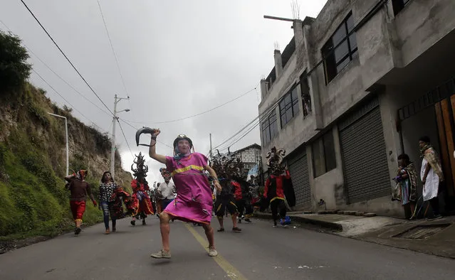 A man dressed in character heads the parade of devils on their way to Pillaro to be part of “La Diablada” festival, in Pillaro Ecuador, Friday, January 6, 2017. The devils wear huge masks, red suits, black cloaks, and elaborate wigs. Some dancers dress as street sweepers while some men wear women's clothes. (Photo by Dolores Ochoa/AP Photo)