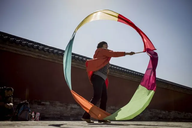 In this picture taken on March 22, 2015, a woman plays with a tricolor ribbon in the grounds of the Temple of Heaven in Beijing. (Photo by Fred Dufour/AFP Photo)