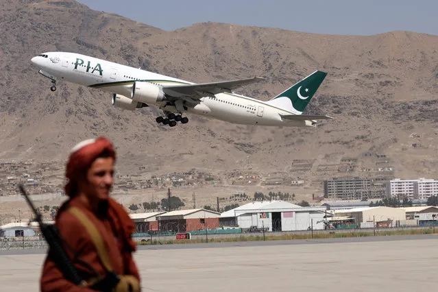 A Taliban fighter stands guard as a Pakistan International Airlines plane, the first commercial international flight to land since the Taliban retook power last month, takes off with passengers onboard at the airport in Kabul on September 13, 2021. (Photo by Karim Sahib/AFP Photo)