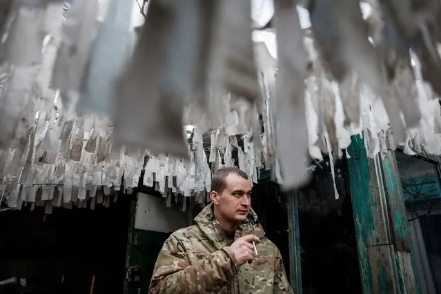 Ihor, a serviceman of the 59th Separate Motorised Infantry Brigade of the Armed Forces of Ukraine, with the call sign “Limuzyn”, smokes under camouflage nets near a frontline, amid Russia's attack on Ukraine, at an undisclosed location in the Donetsk region, Ukraine on February 4, 2024. (Photo by Alina Smutko/Reuters)