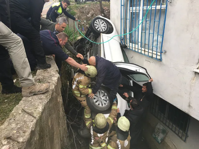 Firefighters team help a man to get out of a car after the driver lost control of the car and it fell in a hole between a sustaining wall and a building in Istanbul, Turkey on March 31, 2018. (Photo by Adem Koc/Anadolu Agency/Getty Images)
