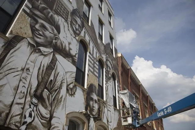 Artist Jason Morgan works on a mural named "Heritage Harvesters" as commissioned by a building owner to depict farmers from the community, Thursday, June 11, 2015, in Wilmington, Ohio. Locals were asked to send photographs of their ancestors who lived in the Wilmington area to adorn the edifice that sits along the town's main drag. (AP Photo/John Minchillo)
