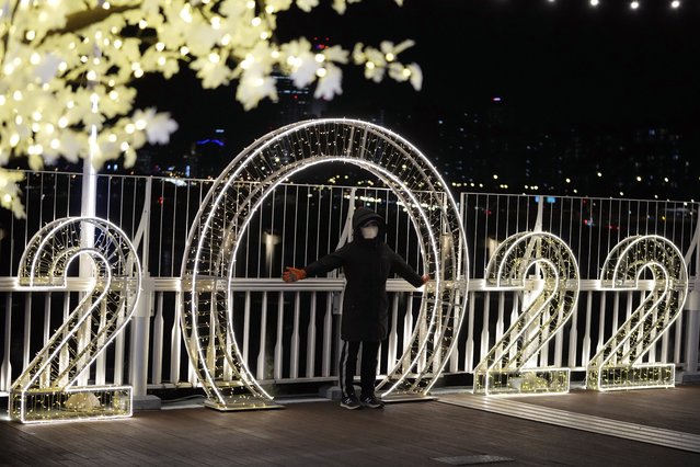 A visitor wearing a face mask poses for a photo in front of an illuminated decorations on New Year's Eve in Seoul, South Korea, Friday, December 31, 2021. (Photo by Lee Jin-man/AP Photo)