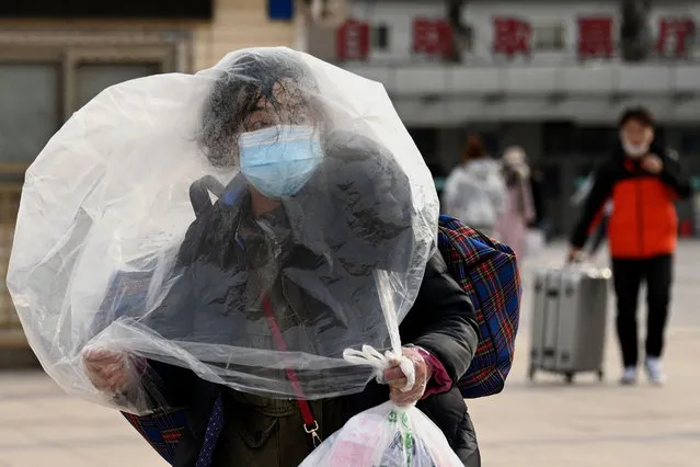 A woman using a plastic bag as a cover walks outside the Beijing railway station in Beijing on January 26, 2022, ahead of the biggest holiday of the year, the Lunar New Year, which ushers in the Year of the Tiger. (Photo by Noel Celis/AFP Photo)