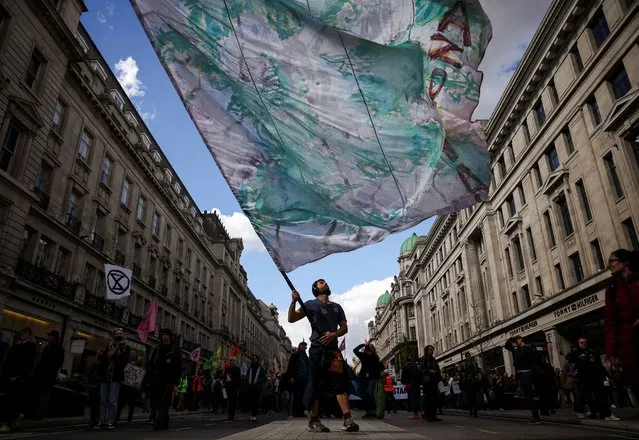 A man holds up a flag as climate activists from Extinction Rebellion take part in a demonstration at Oxford Circus in London, Britain, April 9, 2022. (Photo by Henry Nicholls/Reuters)
