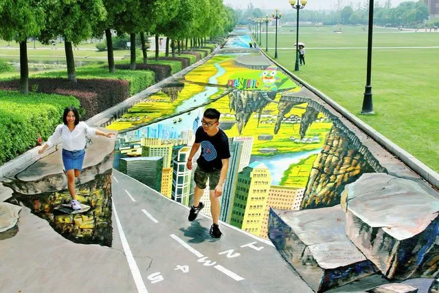 College students pose for pictures with a 3D painting along a street at a campus in Nanjing, Jiangsu province. (Photo by Reuters/China Daily)