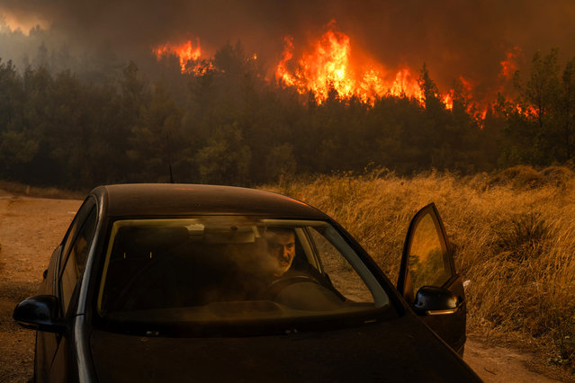 A local gets into his car in front of the flames to evacuate during a wildfire in Dione on August 12, 2024. On August 12, 2024, Greece's civil protection authorities ordered the evacuation of several towns in the north-eastern suburbs of Athens, threatened by a violent fire that started the day before and is spreading. (Photo by Angelos Tzortzinis/AFP Photo)