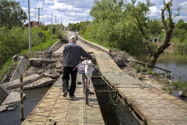 A man pushes his bicycle across a repaired bridge in Vilkhivka, outside Kharkiv, in eastern Ukraine, Friday, May 20, 2022. (Photo by Bernat Armangue/AP Photo)