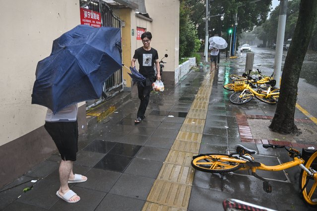 People walk past fallen bicycles amid strong winds and rain from the passage of Typhoon Bebinca in Shanghai on September 16, 2024. The strongest storm to hit Shanghai in over 70 years made landfall on September 16, state media reported, with flights cancelled and highways closed as Typhoon Bebinca lashed the city with strong winds and torrential rains. (Photo by Hector Retamal/AFP)