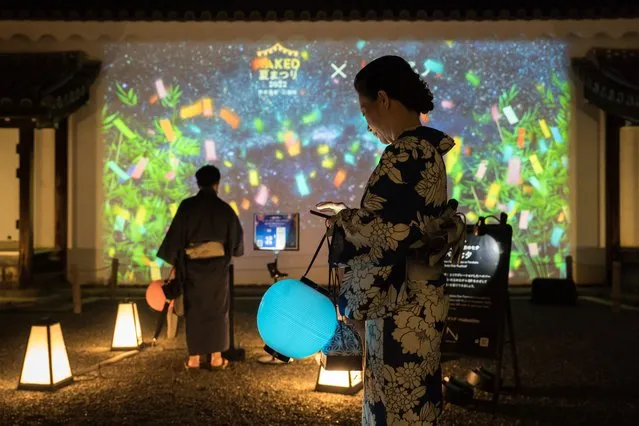 Guest attendees holding lanterns stand in front of a digitally projected image during a preview of the Naked Summer Festival 2022 at Nijo-jo Castle on July 21, 2022 in Kyoto, Japan. (Photo by Tomohiro Ohsumi/Getty Images)