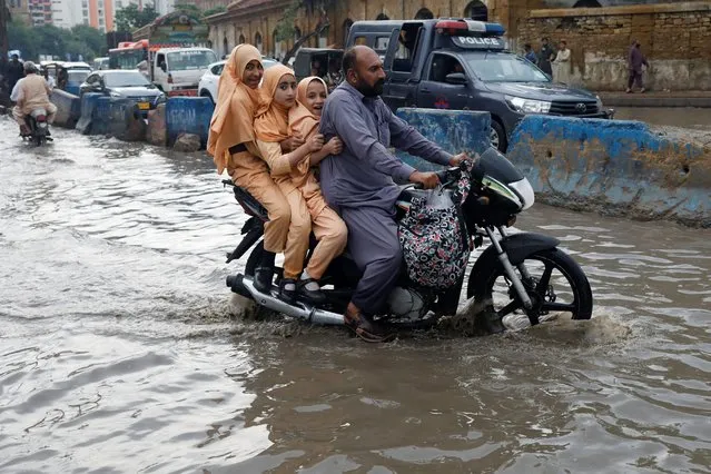 A man and students ride on a motorcycle on a flooded road, following rains during the monsoon season in Karachi, Pakistan on August 10, 2022. (Photo by Akhtar Soomro/Reuters)