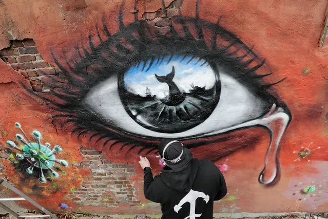 A graffiti artist works on a mural featuring a crying eye surrounded by coronavirus spores on a building adjacent to the Custom House Square in New Bedford, Connecticut on March 30, 2020. (Photo by Peter Pereira/AP Photo)