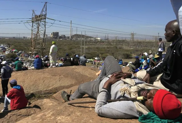 Mine workers sit on a hill during the commemoration ceremonies in Marikana, South Africa, Tuesday, August 16, 2022. A somber gathering of about 5,000 people marked the 10th anniversary of what has become known as the Marikana massacre, when police opened fire on striking miners, killing 34 in 2012. (Photo by Themba Hadebe/AP Photo)