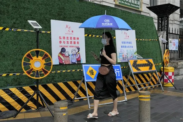 A woman wearing mask walks past construction warning sign during a rainy day in Beijing, Thursday, August 18, 2022. (Photo by Ng Han Guan/AP Photo)
