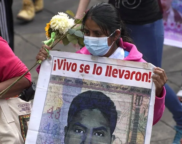 A relative of one of the missing 43 Ayotzinapa college students marches with a sign that has the image of her loved one and the phrase that reads in Spanish “They took him alive”, in Mexico City, Monday, September 26, 2022, on the day of the anniversary of the disappearance of the students in Iguala, Guerrero in 2014. Three members of the military and a former federal attorney general were recently arrested in the case, and few now believe the government's initial claim that a local drug gang and allied local officials were wholly to blame for seizing and killing the students on July 26, 2014, most of which have never been found. (Photo by Marco Ugarte/AP Photo)