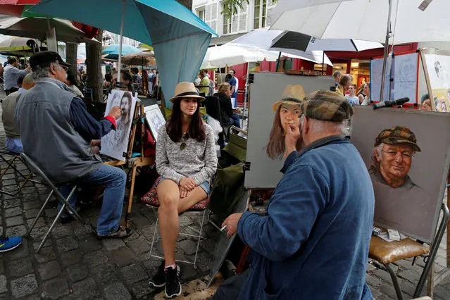 A portrait artist of “Place du Tertre” paints a portrait of a young tourist, close to Montmartre's Sacre Coeur Church in Paris, France August 20, 2016. (Photo by Pascal Rossignol/Reuters)