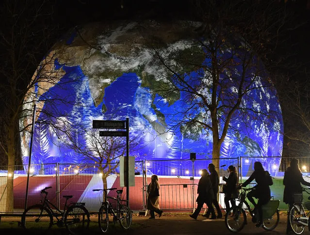 People pass the German pavilion in the shape of the earth during the COP 23 Fiji UN Climate Change Conference in Bonn, Germany, Wednesday evening, November 15, 2017. (Photo by Martin Meissner/AP Photo)