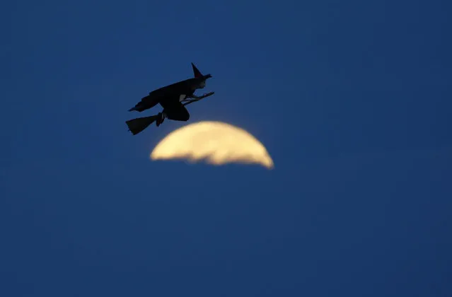 A radio-controlled flying witch makes a test flight past a moon setting into clouds along the pacific ocean in Carlsbad, California October 8, 2014. (Photo by Mike Blake/Reuters)