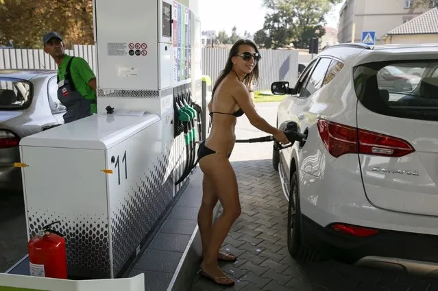 A woman wearing a bikini holds a fuel pump nozzle as she fills up her car with fuel at a petrol station in Kiev, Ukraine, September 26, 2015. (Photo by Valentyn Ogirenko/Reuters)