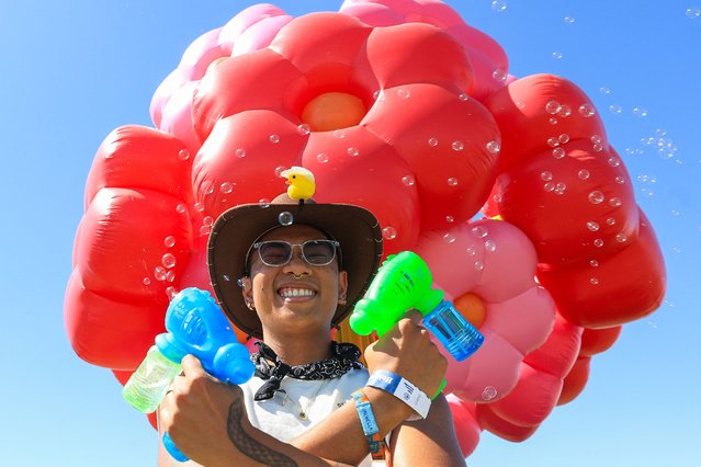 A festivalgoer plays with bubbles as he poses for a photo by French design collective Uchronia's “Le Grand Bouquet” large-scale floral art installation during the 2025 Coachella Valley Music and Arts Festival at Empire Polo Club on April 13, 2025 in Indio, California. (Photo by Valerie Macon/AFP Photo)