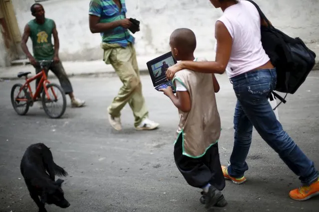 A boy holds a portable video player as he walks with his mother in Havana September 18, 2015. (Photo by Edgard Garrido/Reuters)