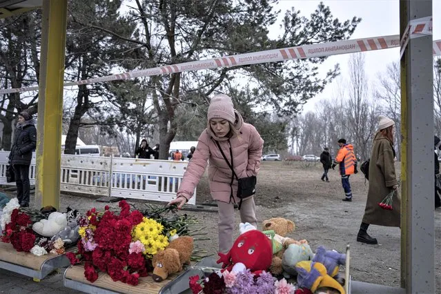 A woman lays flowers at a bus stop, for people who were killed in a Russian missile strike on an apartment building  in the southeastern city of Dnipro, Ukraine, Monday, January 16, 2023. (Photo by Evgeniy Maloletka/AP Photo)