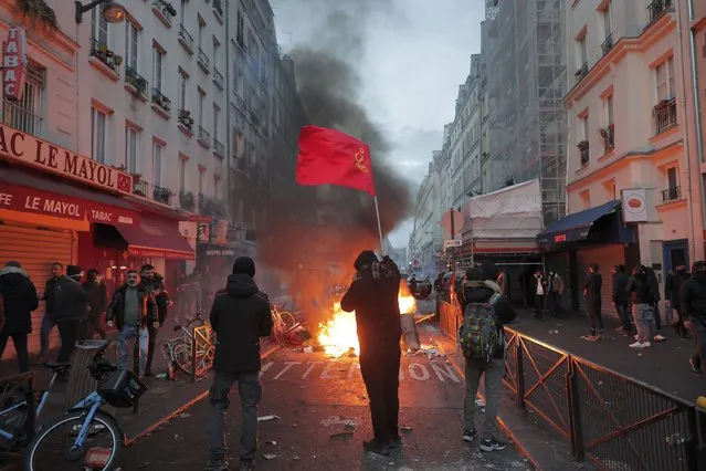 A members of Kurdish community waves the Kurdish communist flags next to a barricade on fire at the crime scene where a shooting took place in Paris, Friday, December 23, 2022. Skirmishes erupted in the neighbourhood a few hours after the shooting, as members of the Kurdish community shouted slogans against the Turkish government, and police fired tear gas to disperse an increasingly agitated crowd. A shooting targeting a Kurdish cultural center in Paris Friday left three people dead and three others wounded. (Photo by Lewis Joly/AP Photo)
