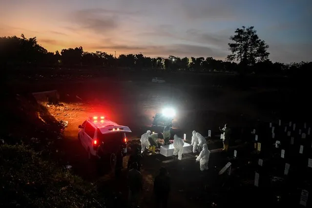 Workers wearing protective suits bury a coronavirus victim at Pondok Ranggon cemetery complex in Jakarta, Indonesia on September 8, 2020. (Photo by Muhammad Adimaja/Antara Foto via Reuters)