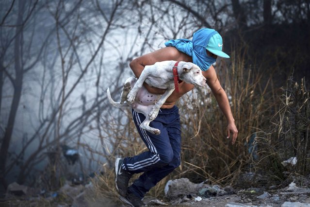 A man, holding a dog, runs from a blaze raging through a neighborhood of Salta, Argentina, Friday, August 1, 2025. (Photo by Javier Corbalan/AP Photo)