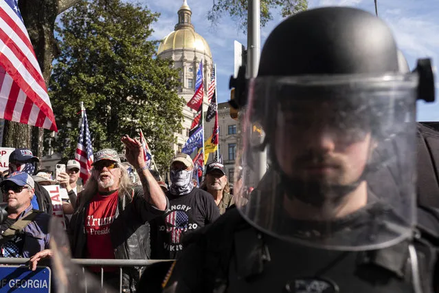 An officer in riot gear stands between supporters of President Donald Trump and counter protesters as the groups yell at each other outside of the Georgia State Capitol in Atlanta on Saturday, November 21, 2020. (Photo by Ben Gray/AP Photo)