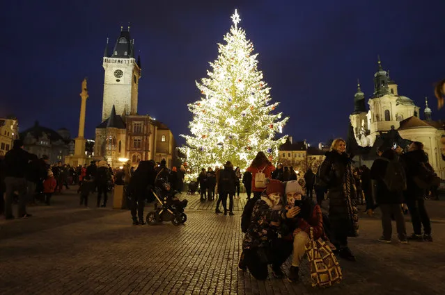 People gather by a Christmas tree illuminating the Old Town Square in Prague, Czech Republic, Saturday, November 28, 2020. Prague city hall has lit up the Christmas Tre but cancelled the traditional Christmas markets due to a record surge in coronavirus infections. (Photo by Petr David Josek/AP Photo)