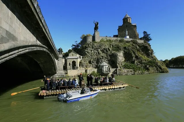 Georgians feast on a raft floating down the Mtkvari River past the ancient Metekhi Church and a monument to Vakhtang I “Gorgasali”, a king of Iberia, during celebrations of the Tbilisoba City Day in Tbilisi, Georgia, Saturday, October 15, 2016. Tbilisoba is an annual October festival, celebrating the diversity and history of Tbilisi, the capital of Georgia. (Photo by Shakh Aivazov/AP Photo)