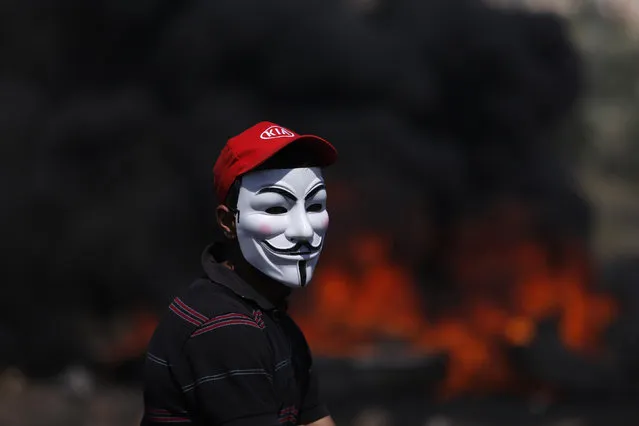West Bank: A Palestinian protester wearing a Guy Fawkes mask stands next to burning tyres during a weekly Friday protest against the Jewish settlement of Qadomem, near the West Bank City of Nablus April 25, 2014. (Photo by Mohamad Torokman/Reuters)