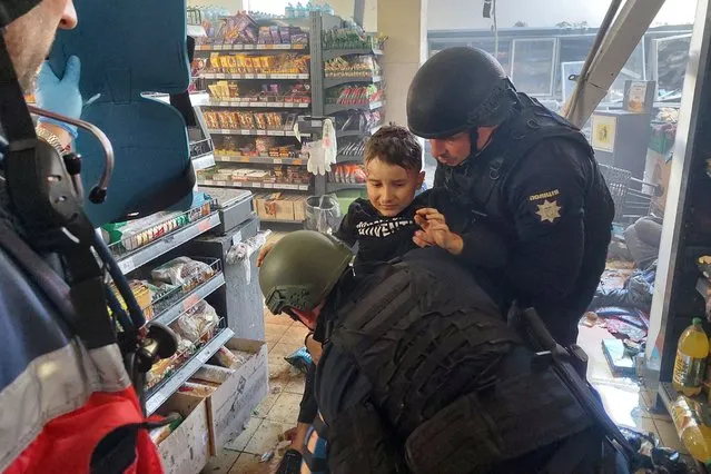 A wounded child is helped by police officers at a local supermarket following a Russian strike in the southern Ukrainian town of Kherson on April 3, 2023, amid the Russian invasion of Ukraine. Russian strikes on Ukraine's southern Kherson region killed 16 people on Wednesday, local prosecutors said as authorities introduced a curfew in the main city of Kherson starting Friday. (Photo by Dina Pletenchuk/AFP Photo)