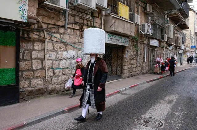 A Jewish man and a girl in Purim costumes walk on the street in the Mea Shearim ultra-Orthodox neighbourhood in Jerusalem, on March 18, 2022. The carnival-like Purim holiday is celebrated with parades and costume parties to commemorate the deliverance of the Jewish people from a plot to exterminate them in the ancient Persian empire 2,500 years ago, as recorded in the Biblical Book of Esther. (Photo by Menahem Kahana/AFP Photo)