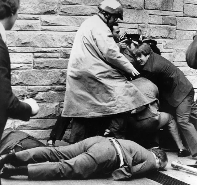 White House press secretary James Brady lies wounded on the sidewalk outside a Washington hotel after being shot during an assassination attempt on U.S. President Ronald Reagan, Monday, March 30, 1981. In the background secret service agents and police wrestle the alleged assailant to the ground. (Photo by Ron Edmonds/AP Photo)