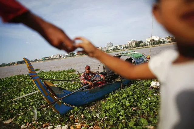 An ethnic Cham Muslim woman sits on her boat on the banks of Tonle Sap river in Phnom Penh July 30, 2013. About 100 ethnic Cham families, made up of nomads and fishermen without houses or land who arrived at the Cambodian capital in search of better lives, live on their small boats on a peninsula where the Mekong and Tonle Sap rivers meet, just opposite the city's centre. The community has been forced to move several times from their locations in Phnom Penh as the land becomes more valuable. They fear that their current home, just behind a new luxurious hotel under construction at the Chroy Changva district is only temporary and that they would have to move again soon. (Photo by Damir Sagolj/Reuters)