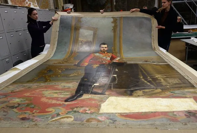 A picture taken in Saint Petersburg on November 17, 2016 shows restorers of the Stieglitz Art and Industry Academy displaying the portrait of Tsar Nicholas II by Ilya Galkin (1896) that was discovered beneath water-soluble paint on the back of the canvas used for the full-size portrait of Vladimir Lenin by Vladislav Izmailovich (1924). A portrait of the last Tsar of Russia, Nicholas II, remained hidden for nearly a century under a portrait of Soviet state founder Vladimir Lenin, and discovered by chance will soon be exhibited in Saint Petersburg, according to restorers. (Photo by Olga Maltseva/AFP Photo)