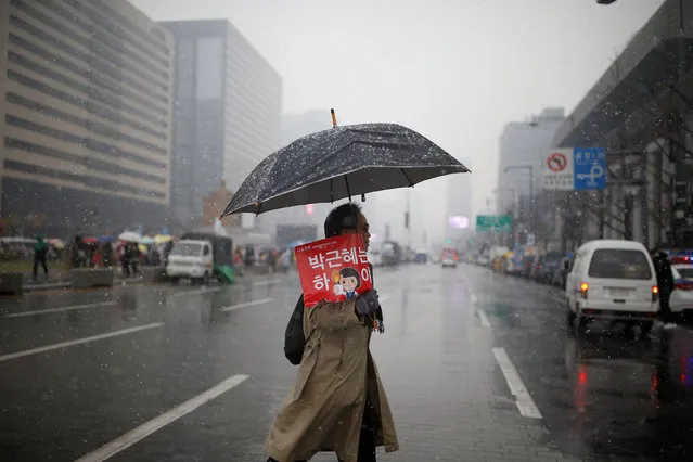 A man holding an umbrella and placard that reads “Step down Park Geun-hye” crosses a road during a protest calling for Park Geun-hye to step down as it snows in Central Seoul, South Korea, November 26, 2016. (Photo by Kim Kyung-Hoon/Reuters)