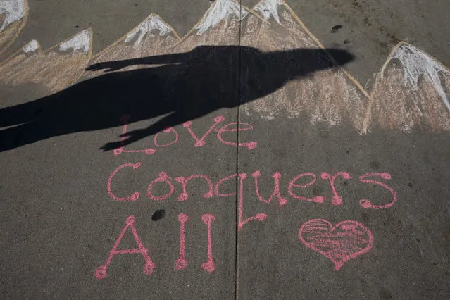 In this November 25, 2016 photo, Kate Bowman, 15, casts a shadow over a chalk message written by her mother on the sidewalk outside the Islamic Center of Claremont in Pomona, Calif. Bowman's father, Harry, was killed in the Dec. 2, 2015, terror attack at the Inland Regional Center in San Bernardino, Calif. Almost a year after his death, Bowman etched the word “love” in yellow chalk on the sidewalk outside a mosque- just one of the messages of peace the teenage Lutheran and her mother have left in an effort to unify Muslims and Christians in the hardscrabble city east of Los Angeles against the violence that many community members feared might divide them. (Photo by Jae C. Hong/AP Photo)
