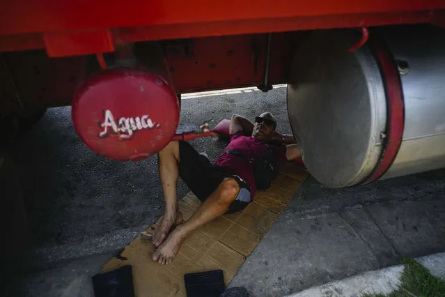 A farm worker sleeps under a truck while waiting in line to refuel his tractor, on the highway to Pinar del Rio, Guanajay, Cuba, Thursday, May 18, 2023. Cuba is in the midst of an acute fuel shortage that has drivers and farmers waiting in line for days or even weeks in order to fuel up their vehicles and tractors. (Photo by Ramon Espinosa/AP Photo)