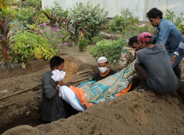 Gayesh Ansari, looks at the body of his 8 months pregnant wife, Gulshan Ansari as he lowers her body into a grave after she died from the coronavirus disease (COVID-19) at a graveyard in Mumbai, India on April 28, 2021. (Photo by Francis Mascarenhas/Reuters)