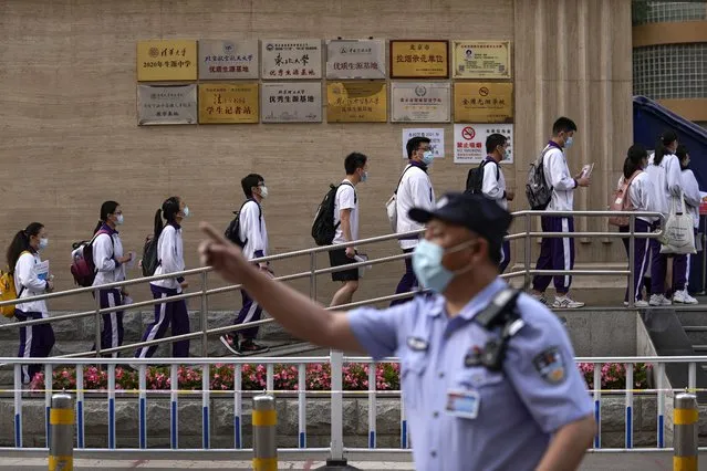 A masked policeman gestures as students wearing face masks to help curb the spread of the coronavirus line up to enter a school for the first day of China's national college entrance examinations, known as the gaokao, in Beijing, Monday, June 7, 2021. More than 10 million high school students throughout China will take the two days annual college entrance exams which started on Monday, according to the state media report. (Photo by Andy Wong/AP Photo)