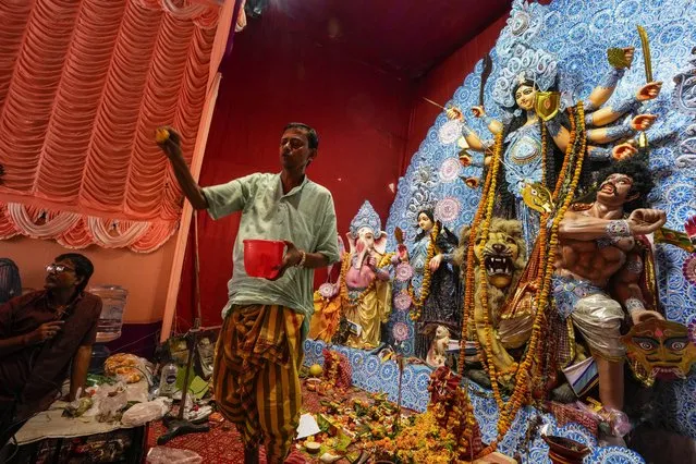 A Hindu priest sprays holy water on the devotees beside the idol of goddess Durga on the second day of Durga Puja festival in Kolkata, India, Sunday, October 22, 2023. The five-day festival commemorates the slaying of a demon king by goddess Durga, marking the triumph of good over evil. (Photo by Bikas Das/AP Photo)