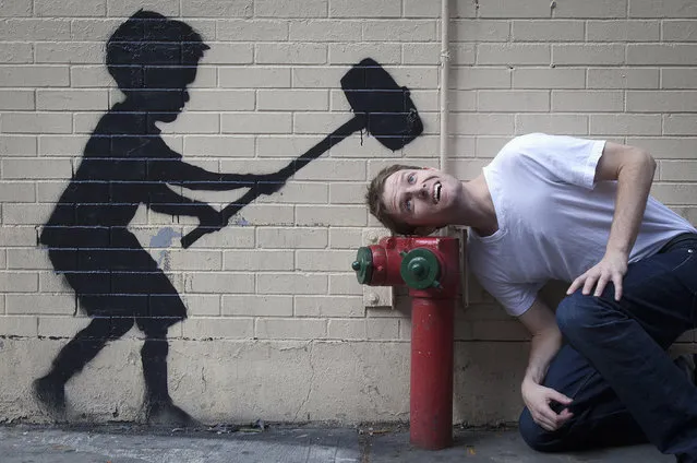 A man jokingly poses with a new installation of British graffiti artist Banksy's art in New York, October 20, 2013. (Photo by Carlo Allegri/Reuters)