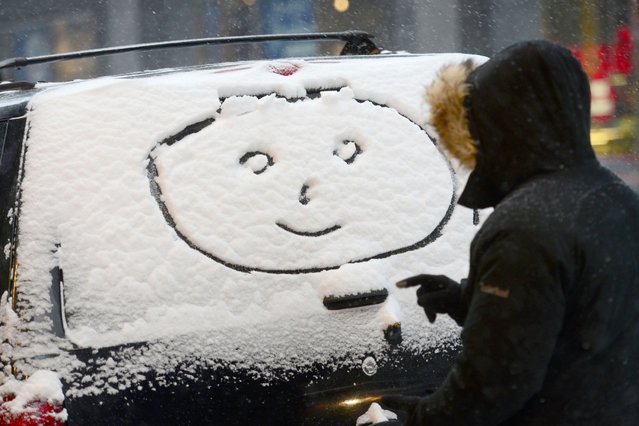 A person makes a "happy face" on a car window during a snow storm in New York, January 21, 2014. In New York, a storm alert was issue for noon (1700 GMT) Tuesday to 6:00 am (1100 GMT) Wednesday with as much as a foot (30 centimeters) forecast for the metropolitan region. (Photo by Emmanuel Dunand/AFP Photo)