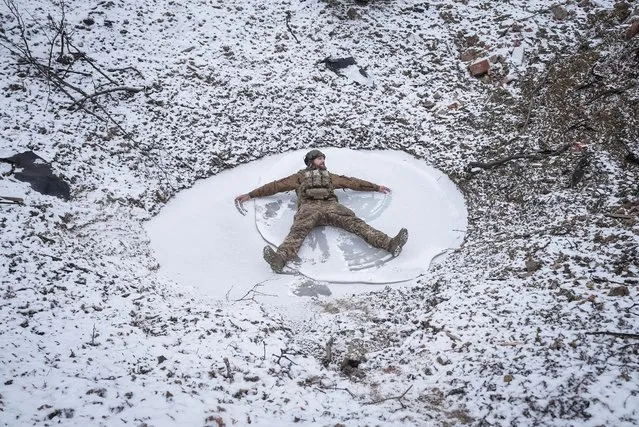 A Ukrainian serviceman of 80th Separate Galician Air Assault Brigade makes a snow angel in a bomb crater, amid Russia's attack on Ukraine, at a position near Bakhmut in Donetsk region, Ukraine on January 25, 2024. (Photo by Inna Varenytsia/Reuters)