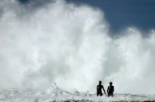 Two boys hold onto a rail at the North Narrabeen Beach rock pool as large waves break towards them on August 25, 2021 in Sydney, Australia. The Bureau of Meteorology has issued severe weather warnings for coastal areas of Sydney and parts of NSW with damaging surf and winds exceeding 100km/h set to batter the state. (Photo by David Gray/Getty Images)